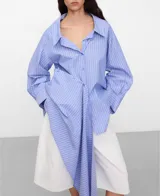 Camisa de algodón con diseño desestructurado a rayas celestes y blancas, cuello camisero, manga larga y cierre frontal de botones.