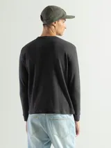 Remera de manga larga con cuello redondo, confeccionada en tejido de algodón tipo mini piqué. Presenta un diseño versátil con puños elásticos en las mangas, ideal para usar como prenda base o como buzo ligero.