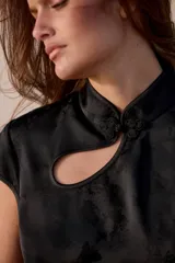 Top satinado color menta con cuello mao, diseño sin mangas, cierre frontal con alamar y detalles de ribetes negros a contraste.