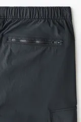 Pantalón cargo gris oscuro de nylon con corte estándar, cintura elástica con cordón ajustable, bolsillos con cierre en los laterales y bolsillos de parche con solapa en las piernas.