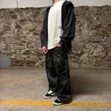 Pantalón de corte super baggy con estampado camuflado en tonos grises y negros, confeccionado en denim con efecto lavado.