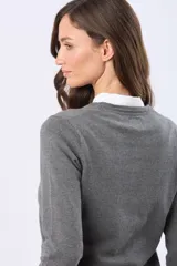 Buzo tejido en hilo de algodón color beige, con cuello redondo y manga larga. Presenta un corte clásico y un pequeño detalle metálico en la parte inferior izquierda.