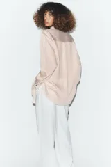 Camisa de corte oversize con estampado de rayas verticales, cuello subido y cierre frontal con botones. Presenta mangas largas con puños y un diseño cruzado en la parte delantera.