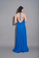 Vestido largo de gasa color azul royal, sin mangas, con escote halter y espalda descubierta en forma de V. Presenta drapeado en la falda y bordado en el escote.
