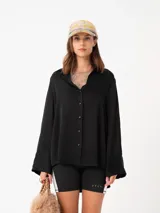 Camisa de raso color negro con silueta suelta, manga larga con puños anchos y cierre frontal de botones a tono.
