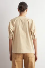 Camisa de manga corta color beige con sutiles rayas verticales blancas, cuello mao y cierre frontal oculto con botones.