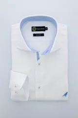 Camisa blanca de algodón con cuello italiano y corte slim fit. Detalle de interior de cuello y cartera en color celeste. Logo de pájaro bordado en el frente.