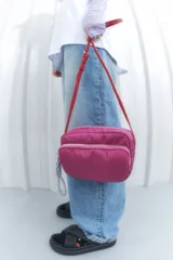 Bandolera fucsia de nylon con correa roja ajustable y dos compartimentos con cierre.