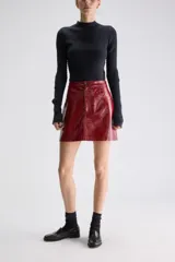 Minifalda evasé de tiro alto, confeccionada en material sintético de acabado brillante, estilo charol, con diseño de cinco bolsillos y cierre frontal con botón y cremallera.