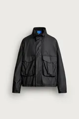 Cazadora regular fit de Zara en colaboración con Aaron Levine, confeccionada en tejido de algodón con acabado efecto encerado en color negro. Presenta cuello subido, manga larga con puño ajustable, bolsillos frontales con solapa y cierre de cremallera oculto con solapa de botones a presión.