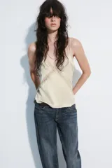 Top de satén color beige con escote en pico, tirantes finos y detalles de encaje aplicado en los bordes y formando una cruz en el frente.