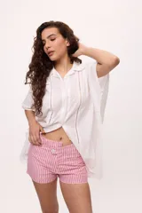 Camisa de manga corta color terracota, con cuello clásico y cierre frontal de botones. Presenta detalles de calados verticales a lo largo del frente y en los laterales, con un corte holgado y fluido.