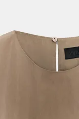 Top de nylon color tostado, con cuello redondo, mangas cortas y bajo abullonado ajustable con cordón y stoppers. Presenta cierre en la espalda con botón.