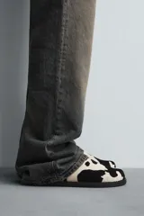 Zueco de piel con pelo con estampado de vaca en blanco y negro. Presenta una horma redonda y una suela de goma negra con volumen.