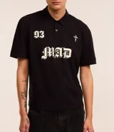 Remera de corte boxy confeccionada en algodón, con cuello polo y cierre frontal de botones. Presenta un diseño estampado en el frente con el número 93, una cruz y la palabra MAD en tipografía gótica.