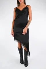 Vestido midi de satén negro, corte lencero, con escote en V adornado con encaje negro. El ruedo es asimétrico y también presenta un borde de encaje.