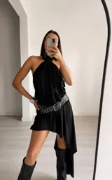 Vestido corto negro con escote halter y diseño asimétrico, con una caída más larga en la parte posterior. Presenta un corte holgado y fluido.