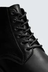 Bota de cuero negro con cordones tipo derby, parte superior lisa y plantilla interior de piel. Presenta horma cuadrada y suela con ligero tacón.