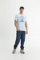Remera de algodón color celeste, con cuello redondo, manga corta y estampa frontal con diseño de volcán y texto.