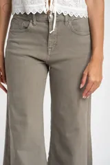 Jean de corte wide leg y tiro medio, en color gris topo. Presenta un diseño de pierna ancha con ruedo desflecado y cierre frontal con botón y cremallera.