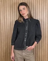 Camisa de denim color negro con efecto gastado, cuello alto con volados sutiles, mangas tres cuartos abullonadas en los hombros y cierre frontal con botones metálicos y costuras pespunteadas en contraste.