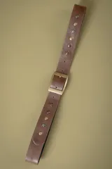 Cinto de cuero marrón con hebilla metálica rectangular y apliques decorativos de estrellas y tachas metálicas en tonos dorados y plateados.