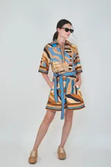 Vestido corto de algodón con estampado geométrico a rayas en tonos marrón, celeste, azul y negro, con cuello camisero, mangas tres cuartos y cinturón ajustable del mismo género.