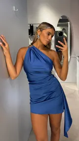 Vestido corto de satén color azul, con diseño de un solo hombro y detalle de frunces laterales que crean un efecto drapeado, finalizando en una caída lateral asimétrica.