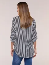 Camisa de corte clásico y silueta relajada con diseño de rayas verticales en blanco y negro. Presenta cuello camisero tradicional, cartera frontal con botones, un bolsillo aplicado en el pecho con rayas horizontales y mangas largas con sistema para arremangar.