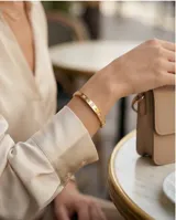 Esclava rígida de acero con baño de oro, diseño tipo brazalete con incrustaciones de circonias brillantes y detalles grabados.