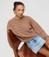 Sweater de punto color marrón, con textura de rayas horizontales formadas por puntos calados. Presenta cuello redondo y mangas largas con puños y ruedo acanalados.