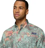 Camisa de manga corta Columbia modelo Super Tamiami, con estampado tropical de hojas en tonos verdes, rosados y naranjas. Presenta cuello abotonado, cierre frontal con botones y bolsillo en el pecho con logo de la marca.