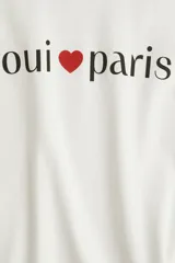 Remera de manga corta color blanco roto, con cuello redondo y estampado central con el texto "oui ❤ paris" en color negro y rojo.