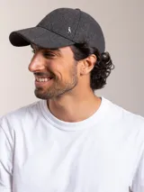 Gorro con visera color gris oscuro, con textura de tweed y un pequeño logo metálico de un pingüino en el lateral.