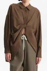 Camisa de manga larga color marrón, con cuello camisero y botones frontales. La prenda se anuda en la parte inferior central, dejando ver parte del abdomen.