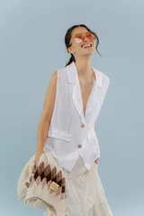 Chaleco de lino blanco con solapas clásicas, cierre frontal de dos botones y bolsillos laterales con solapa. Presenta un corte holgado y sin mangas.