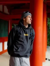 Hoodie gris oscuro con capucha, corte boxy y bolsillo tipo canguro. Presenta un pequeño estampado frontal con tres cuadros amarillos que contienen cruces negras.