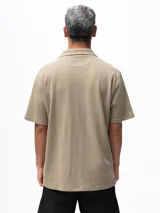 Camisa de manga corta color beige, confeccionada en tejido piqué de algodón, con cuello cubano y un bolsillo de parche en el pecho.