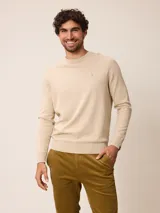 Sweater de punto cuello redondo en color beige, con mangas largas y puños y ruedo acanalados. Cuenta con un pequeño bordado sutil en el pecho.
