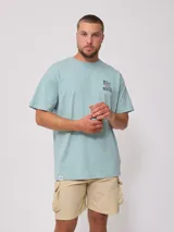 Remera de algodón color celeste pálido, corte oversize, con cuello redondo y manga corta. Presenta un pequeño estampado en el pecho con el texto "RUSTY MANTRA".