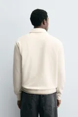 Polo de manga larga color gris oscuro, con diseño de textura estructurada, cuello solapa y cierre frontal de cremallera corta. Cuenta con puños y cintura de rib elástico.