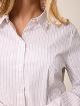 Camisa de corte clásico y calce entallado, color blanco, con cuello camisero, cierre frontal de botones y mangas largas con puños abotonados. Presenta un pequeño bordado distintivo en el pecho.