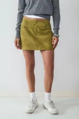 Pollera mini color verde oliva con efecto desgastado, dos bolsillos delanteros y cierre oculto. Confeccionada en tejido plano.