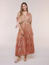 Vestido largo de gasa color salmón con un sutil patrón estampado brillante en tono dorado. Cuenta con escote en V cruzado, cintura imperio elastizada y mangas cortas con tiras ajustables terminadas en borlas.