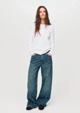 Jeans de tiro medio y corte barrel con diseño de ojales metálicos distribuidos por toda la prenda. Cuenta con cinco bolsillos, cierre de botón y cremallera, y trabillas para cinturón.