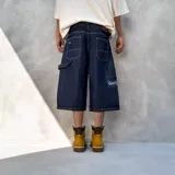 Bermuda de jean estilo baggy, confeccionada en denim de algodón premium con textura rústica. Presenta un diseño de corte amplio, costuras reforzadas en contraste y un bordado distintivo en la parte inferior de la pierna.
