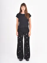 Jean de corte recto y tiro alto, color negro, con diseño de ojales metálicos distribuidos por toda la prenda.