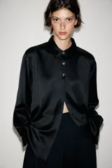 Camisa de satén color blanco, de corte clásico con cuello solapa, manga larga con puños y cierre frontal con botones dorados.