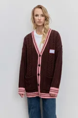 Cardigan de punto con diseño de bloques de color, combinando azul marino en el cuerpo y beige en las mangas. Presenta un tejido con textura de trenzas, cuello en V con borde rayado en azul y blanco, cierre frontal con botones y bolsillos delanteros. Incluye un parche decorativo en el pecho.