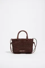 Minibolso marrón de Bimba y Lola, confeccionado en piel vacuna con diseño trenzado y estructura rígida. Cuenta con asas de mano trenzadas, correa de hombro ajustable y etiqueta frontal con el logo de la marca.